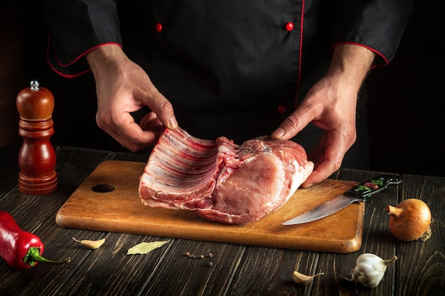 Experienced chef is holding a piece of raw meat with a bone in the kitchen