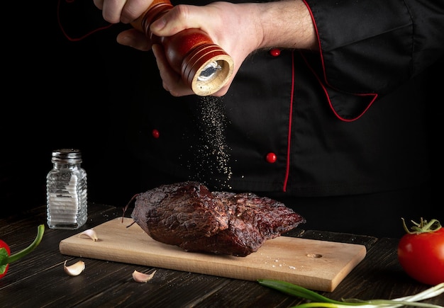 Experienced chef sprinkles the baked beef meat with pepper Working environment on the kitchen table