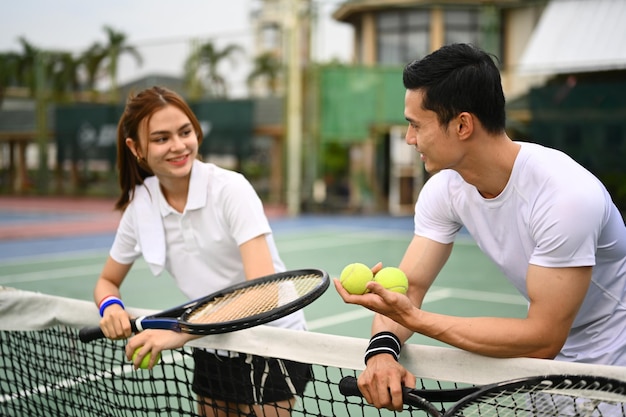 Experienced male tennis coach giving instructions to his student standing by net at the outdoor tennis court