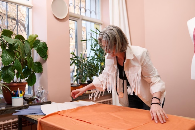 Experienced tailor spreads a luxury tissue on a wooden table before transferring sewing pattern while creating new garment in a fashion design studio