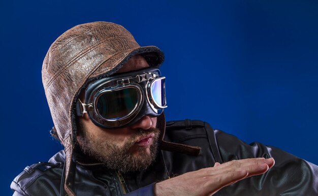 Explore pilot of the 20s with sunglasses and vintage aviator helmet. Wears leather jacket, beard and expressive faces