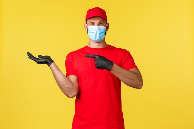 Express delivery during pandemic, covid-19, safe shipping, online shopping concept. Happy good-looking courier, enthusiastic delivery employee in uniform, pointing at hand holding your product