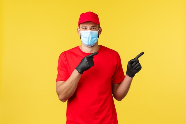 Express delivery during pandemic, covid-19, safe shipping, shopping concept. Friendly courier in red uniform, medical mask and gloves, inform clients about safe contactless deliver, point right