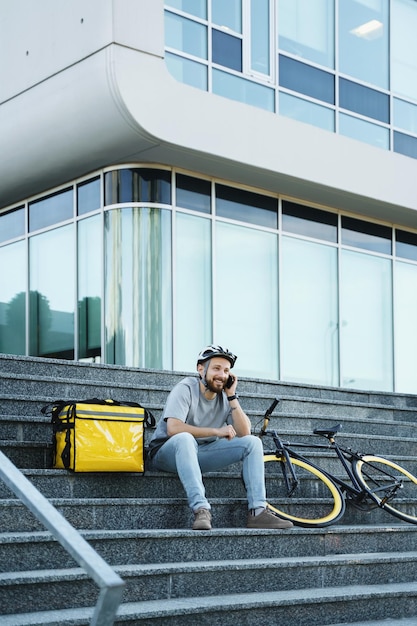 Express food delivery courier sitting on the stairs with insulated bag and bicycle