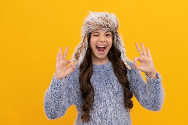 Express positive emotion. winter fashion. ok. cheerful kid with curly hair in earflap hat.