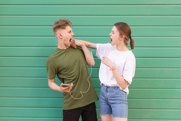 Expressive amusing couple listening to music in headphones on a green