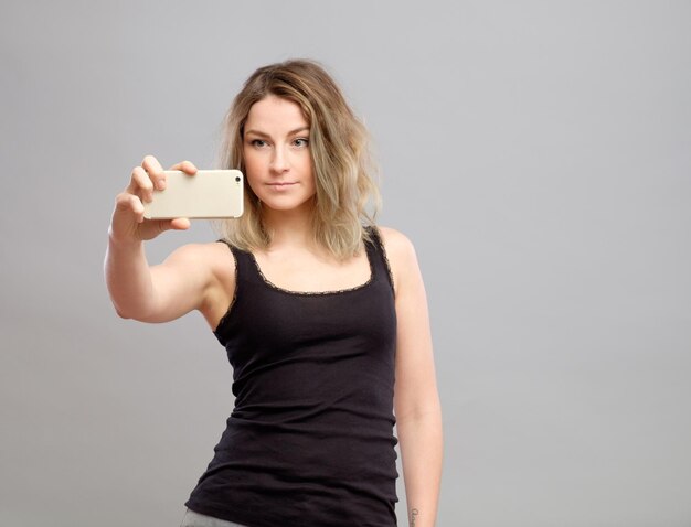 Expressive young woman taking pictures through cellphone over gray background