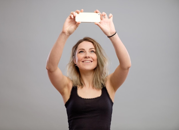 Expressive young woman taking pictures through cellphone over gray background