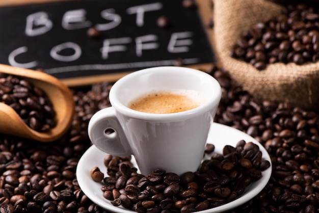 Expresso coffee cup close-up over dark roasted coffee beans