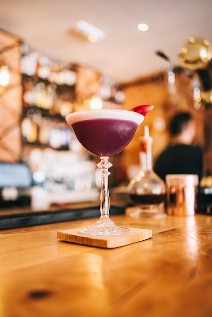 Exquisite maroon cocktail in a special glass on a wooden bar counter against the background of a bar