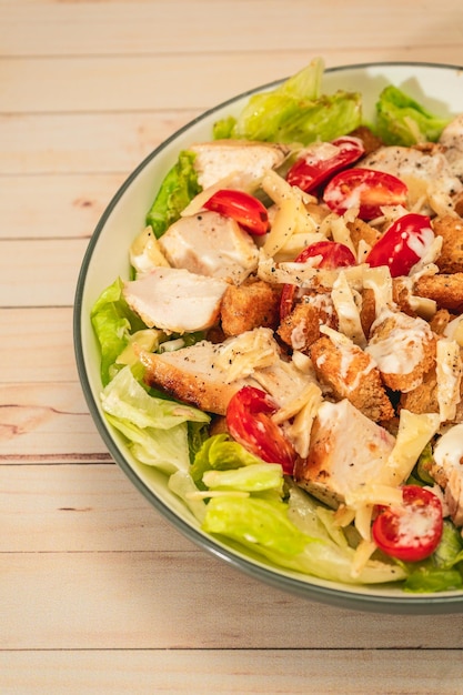 Exquisite variation of Caesar salad with small bites of chicken cherry tomatoes and a gourmet aioli sauce in a small bowl on a wood table Top viewvertical orientation Natural food