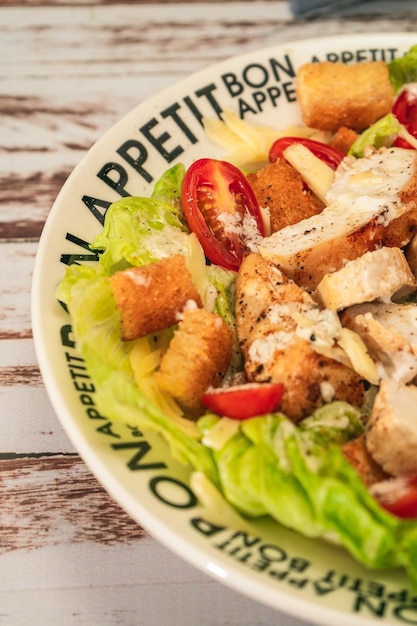 Exquisite variation of Caesar salad with thin slices of chicken cherry tomatoes and a gourmet aioli sauce in a small bowl on a rustic table High view Vertical orientation Close up