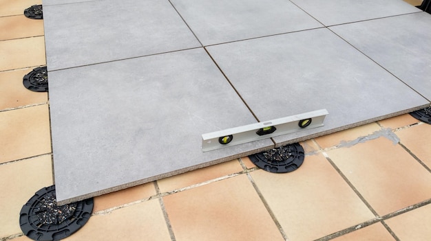 Exterior pavement tiles installation on the house terrace with bubble level and adjustable plots plastic studs