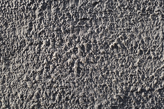 Exterior rough uneven gray wall, decorative dark plaster, textured surface outdoor background.