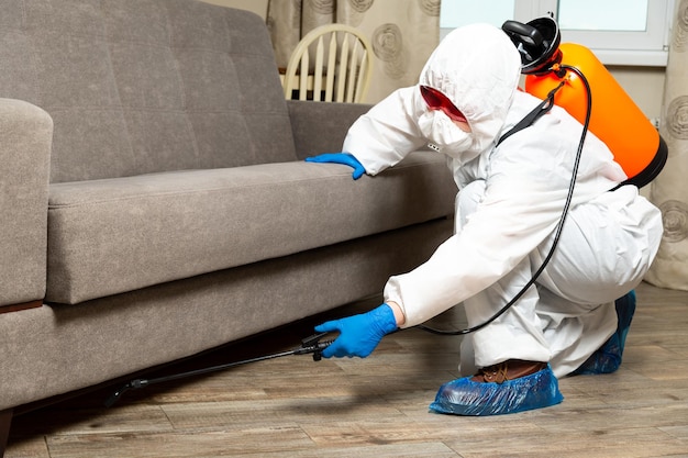 An exterminator in work clothes sprays pesticides with a spray gun. Fight against insects in apartments and houses. Disinsection of the premises