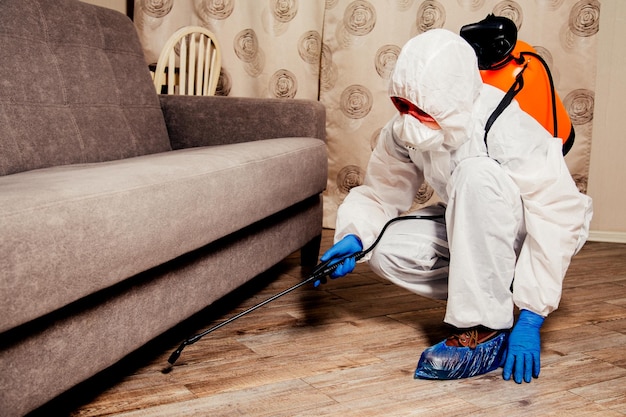 An exterminator in work clothes sprays pesticides with a spray gun. Fight against insects in apartments and houses. Disinsection of the premises