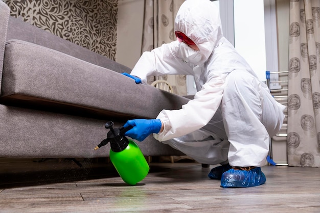 An exterminator in work clothes sprays pesticides with a spray gun Fight against insects in apartments and houses Disinsection of the premises