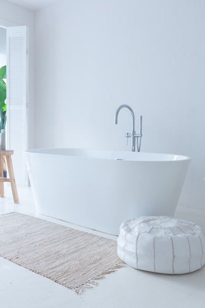 Extra white and very light minimalistic stylish elegant interior of bathroom with modern bath, green plants and wooden elements