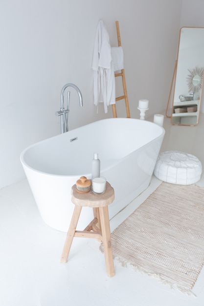 Extra white and very light minimalistic stylish elegant interior of bathroom with modern bath, green plants and wooden elements