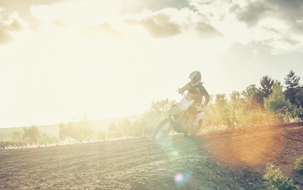 Extreme Motocross MX racer accelerating in dirt track at bright sunset