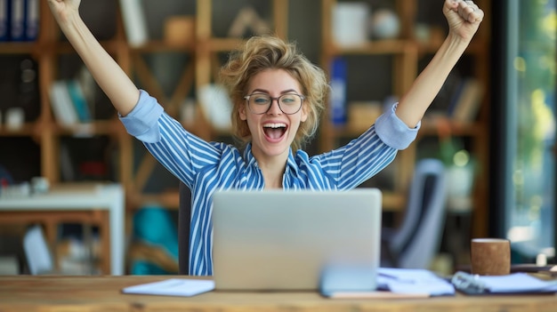 exuberant woman with tousled hair and glasses is raising her arms triumphantly in front of a laptop expressing joy and success