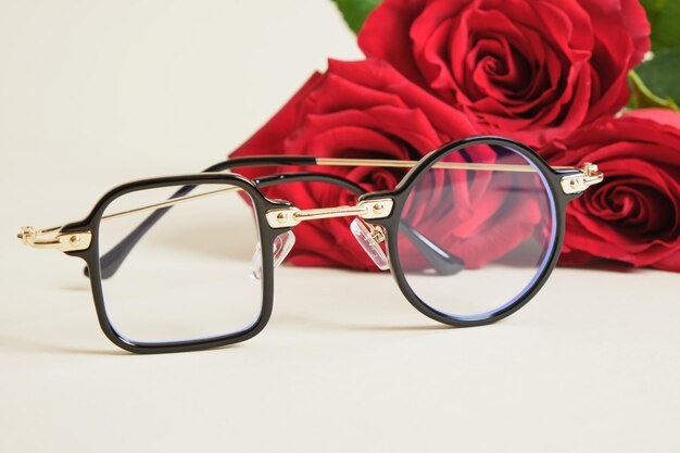 Eye glasses and red roses on beige background