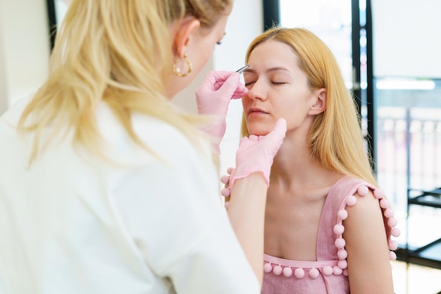 The eyebrow master plucks the hairs from a female client Luxury beauty salon