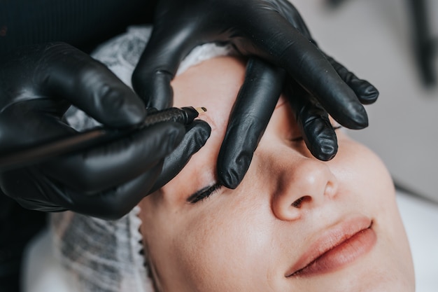 Eyebrows microblading concept. Cosmetologist preparing young woman for eyebrow permanent makeup procedure.