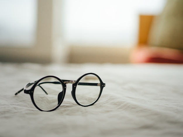 Eyeglasses on white bed in the morning.