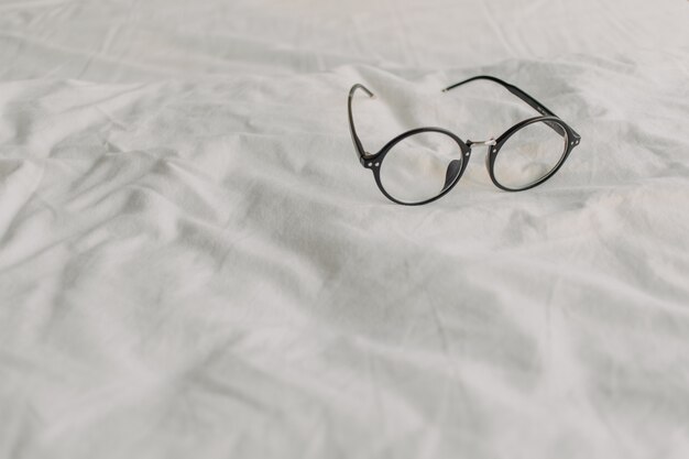 Eyeglasses with black plastic temple on white bed sheet.