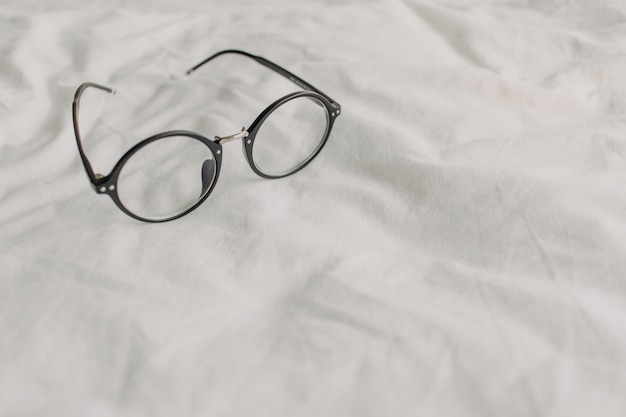 Eyeglasses with black plastic temple on white bed sheet.