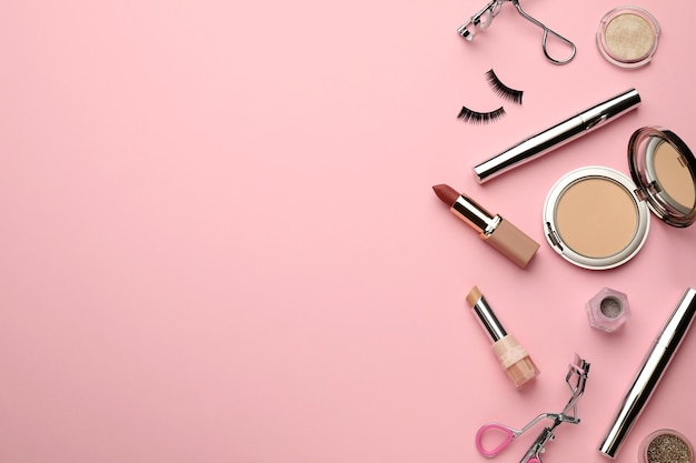 Eyelash curlers and makeup products on pink background flat lay Space for text