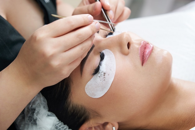 Eyelash extension procedure with tweezers in beauty salon