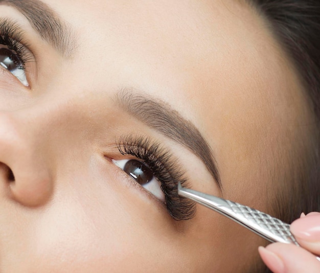 Eyelash extensions. a young woman undergoes a close-up eyelash extension procedure. Tweezers.