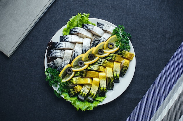 On fabric dark background on a plate beautiful herring and mackerel