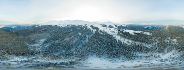 Fabulous evening panorama with snow-capped mountains and hills with bright sun and fog on a frosty winter evening. Beautiful harsh northern nature concept. Copyspace