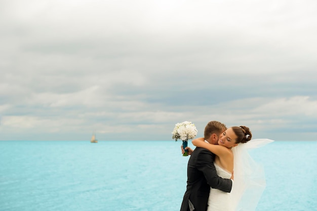 Fabulous newlyweds are holding each other on the sea background the bride is smiling