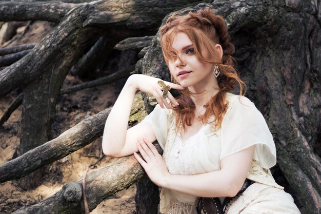 Fabulous red-haired woman near the roots of a tree