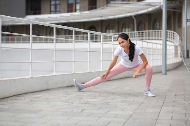 Fabulous tanned fit girl wearing sport clothes doing stretching workout at the stadium. Space for text