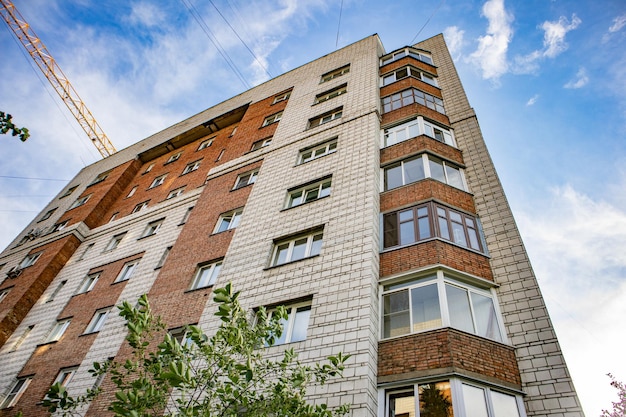 The facade of a modern residential brick house and the boom of a construction crane the concept of housing construction and real estate investment