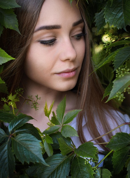 Face of beautiful young woman with clean perfect skin covered by leaves Portrait of beauty model with natural nude make up and long eyelashes Spa skincare and wellness Close up