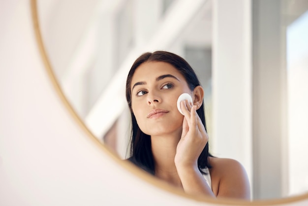 Face beauty and mirror with a woman cleaning her skin in the bathroom of her home in the morning Skincare reflection and cosmetics with an attractive young female going through her facial routine