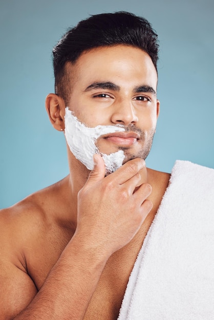 Face beauty and shave with a man model in studio on a blue background for shaving or grooming Portrait skincare and hair removal with a handsome young male shaving his beard in the bathroom