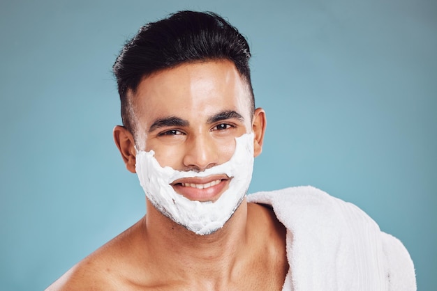 Face beauty and shaving with a man model in studio on a blue background for wellness or grooming Portrait skincare and hair removal with a handsome young male in the bathroom to shave his beard