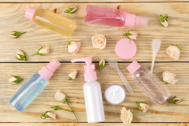 Face and body cosmetics in pink bottles with fresh roses on a natural wooden background. creams and lotion. spa. top view