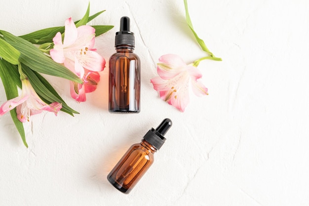 Face and body skin care product essential oil serum in two cosmetic bottles with a dropper on a white background with astromeria flowers Top view