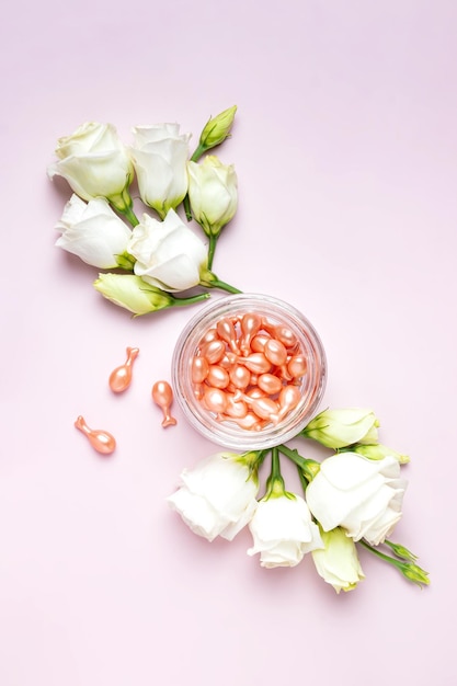 Face care oil capsules on pink background single use nourishing oil for dry and damaged skin antiage therapy daily beauty routine Pink background with white flowers composition