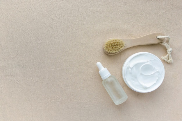 Face care products. Massage brush, cream and serum on beige background, space for text.