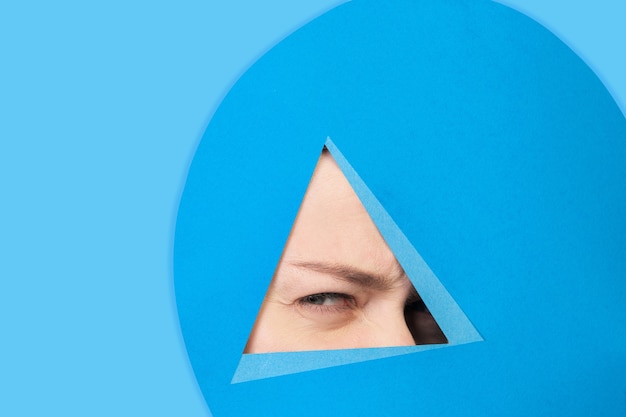 Face of caucasian woman peeking throught triangle in blue background