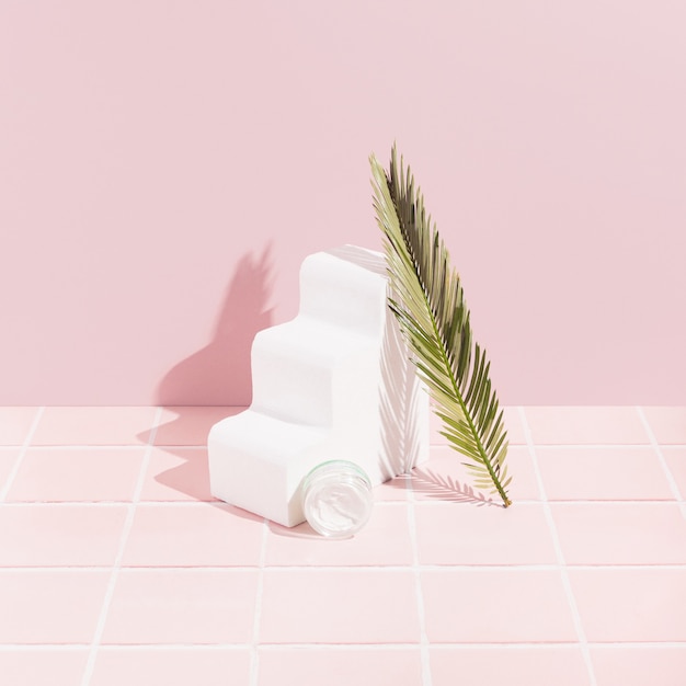 Face cream and green leaf on pastel pink background with tiles. One white wavy 3d object. Natural make up or cosmetics beauty product style.